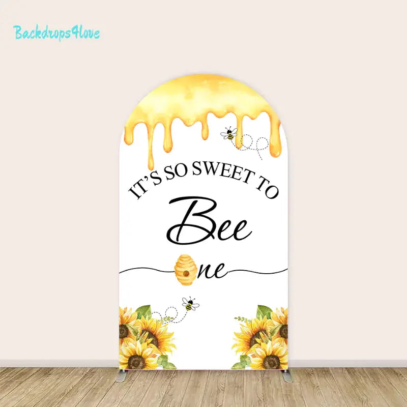 Centerpiece arched backdrop with the phrase 'It’s So Sweet to Bee One,' dripping honey, and a decorative beehive accent.