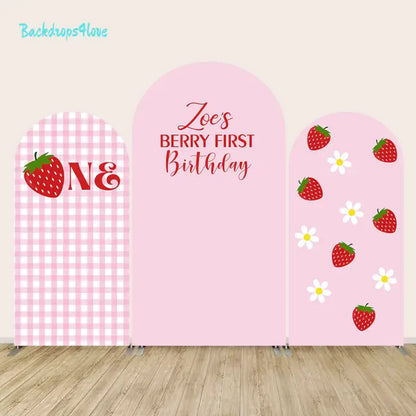 Arch backdrop set with various strawberry designs and a gingham background for first birthday celebration