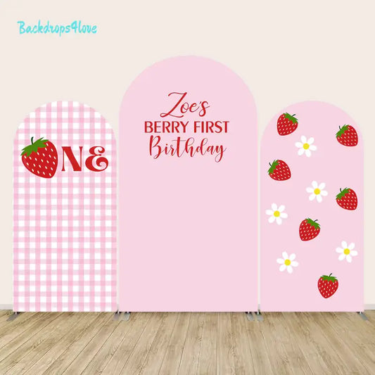 Arch backdrop set with various strawberry designs and a gingham background for first birthday celebration