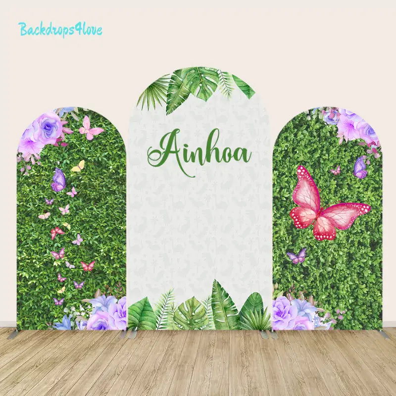 Set of three arches with greenery, butterflies, and floral designs, including a central arch with 'Ainhoa' text