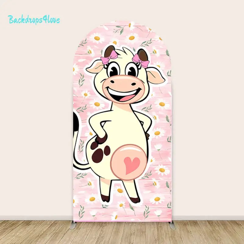 A cheerful cartoon cow with big eyes, pink bows on its ears, and a pink heart on its belly stands against a pastel pink floral backdrop decorated with white daisies and green leaves. The design is bright, playful, and kid-friendly, suitable for celebrations or events.