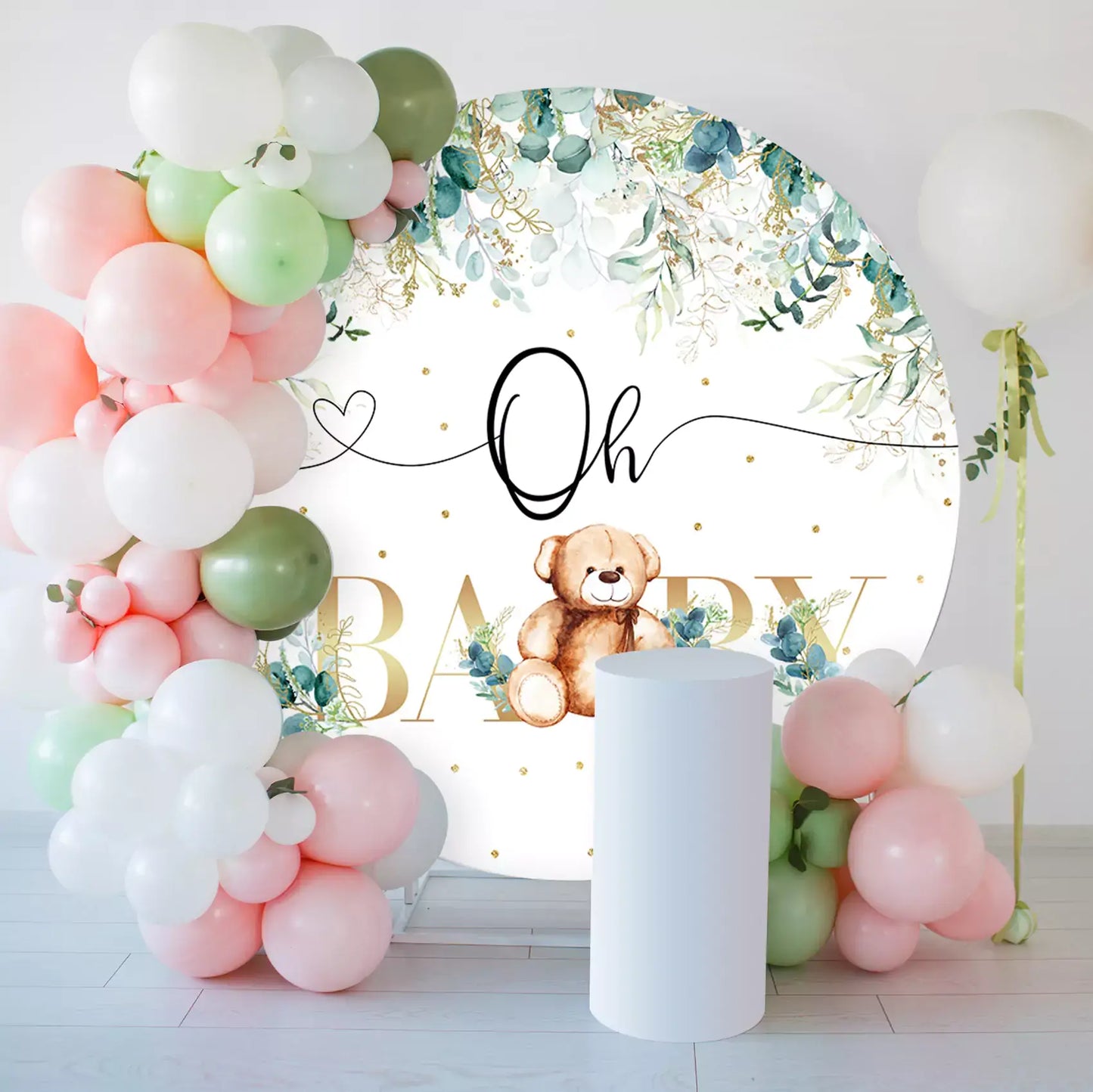 Round backdrop featuring eucalyptus greenery, a teddy bear, and gold glitter text that says "Oh Baby Bear"