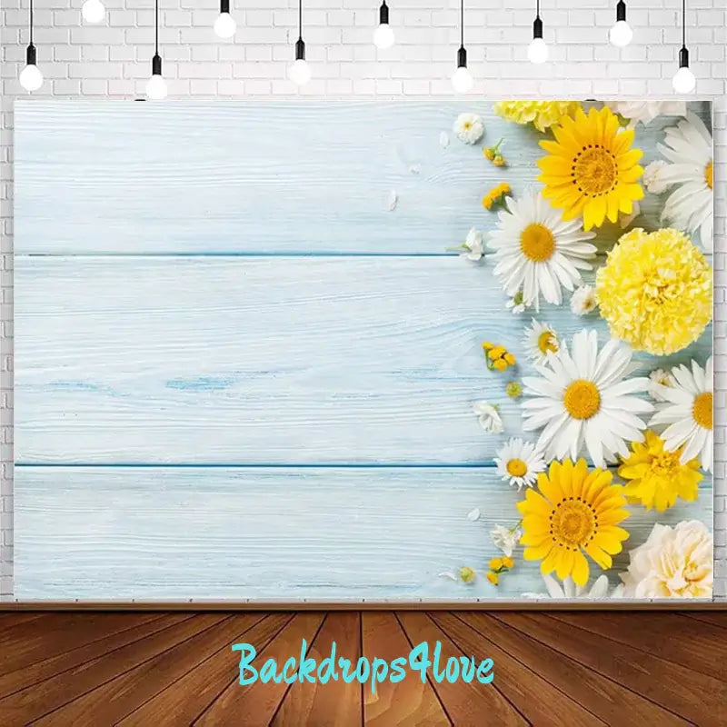 A rustic wooden plank backdrop with yellow and white flowers, including daisies, arranged along the right side. Perfect for spring-themed events or floral decor at garden parties and celebrations.