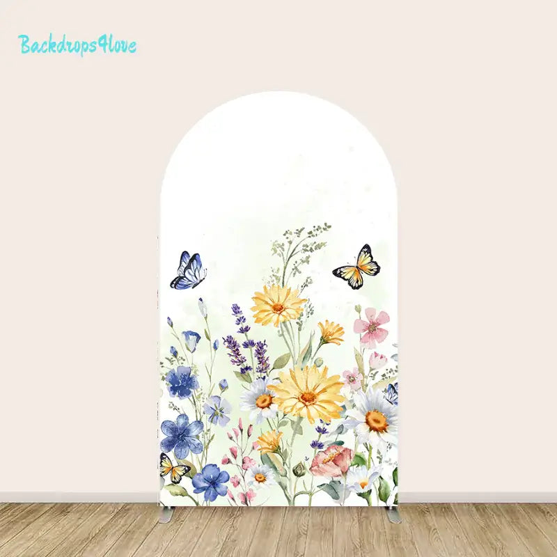 A decorative arched backdrop featuring an arrangement of colorful wildflowers, including daisies and lavender, with butterflies fluttering around. The flowers are in shades of yellow, blue, pink, and purple against a light, pastel green background. The scene has a soft and natural aesthetic.