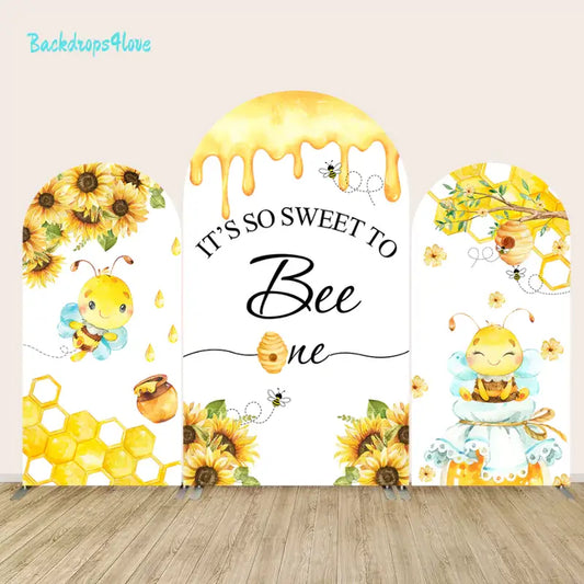 Three-piece arched backdrop set featuring a bee and sunflower theme with honeycomb details, dripping honey, and the phrase 'It’s So Sweet to Bee One.