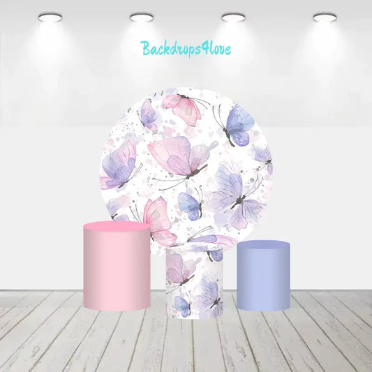 A pastel butterfly-themed decor set featuring a round backdrop with pink, purple, and blue butterflies and cylinder covers in matching pastel shades of pink and blue.