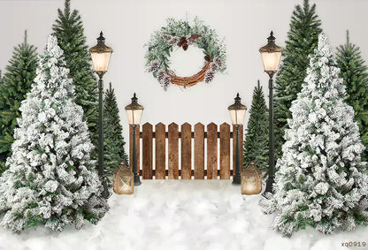 Photography backdrop featuring a winter wonderland scene with frosted Christmas trees, vintage lanterns, a wooden fence, and a festive wreath, perfect for holiday parties and events.